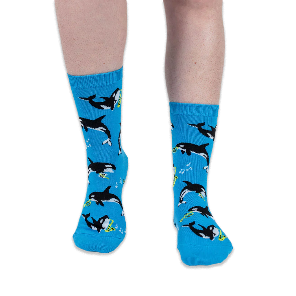 Front view of someone wearing bright blue crew socks with an orca and musical instrument pattern against a black background.