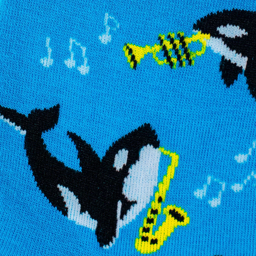 Close-up of the blue knit sock fabric detailing a black and white orca playing a yellow saxophone near white music notes.