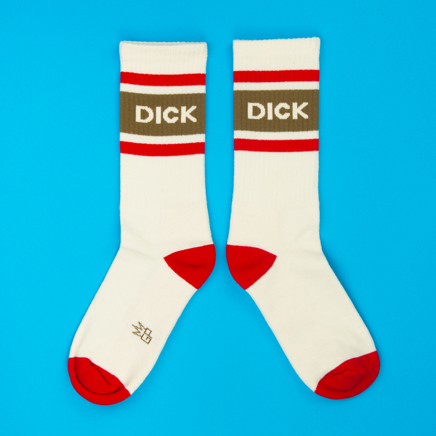 Two cream crew socks laid flat on a blue background, each with a brown "DICK" band and red accents.