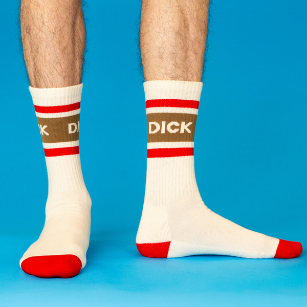 [lf] Person's legs wearing cream crew socks with "DICK" text on a brown band and red striped cuffs and toes, on a blue background.