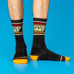 A person wears the black 'Good Grief' crew socks, showing the design and orange toe/heel against a blue background.