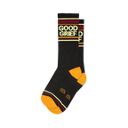 A folded pair of black crew socks featuring 'Good Grief' text, orange toe and heel, and burgundy, gold, and cream stripes.