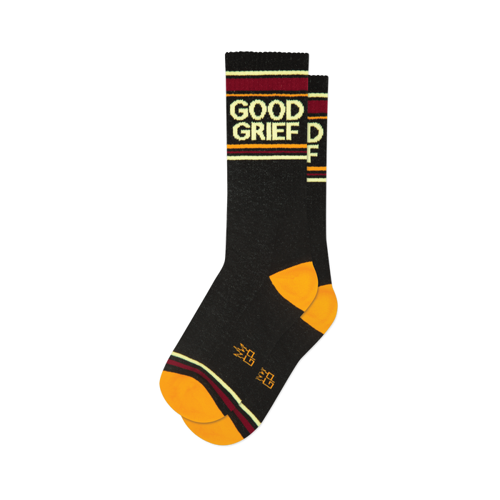 A folded pair of black crew socks featuring 'Good Grief' text, orange toe and heel, and burgundy, gold, and cream stripes.