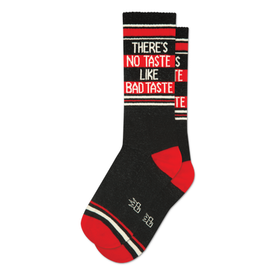 Single dark grey crew sock with "THERE'S NO TASTE LIKE BAD TASTE" text, red heel, red toe, and white/red stripes.