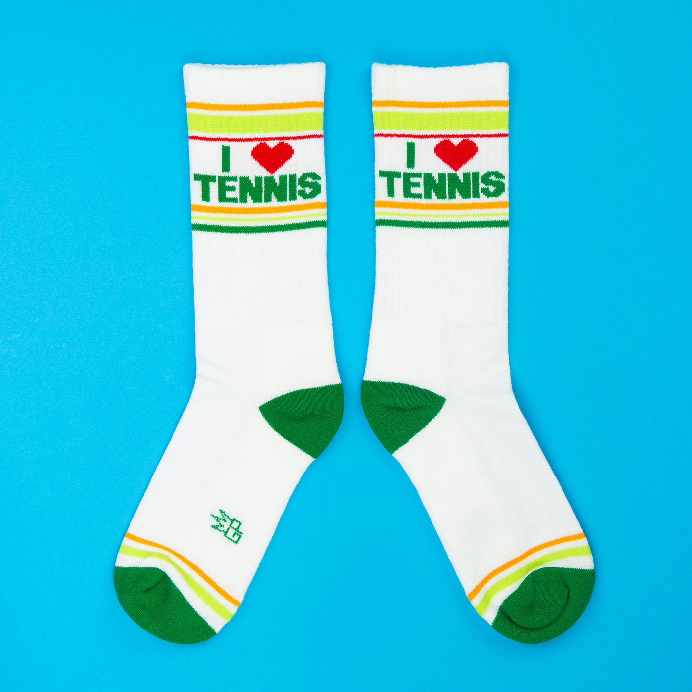 Pair of white 'I ❤️ Tennis' crew socks with green, yellow stripes, green heels and toes, displayed on blue background.