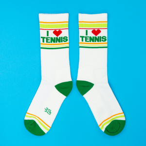 Pair of white 'I ❤️ Tennis' crew socks with green, yellow stripes, green heels and toes, displayed on blue background.