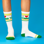 Two legs wearing white 'I ❤️ Tennis' crew socks with green text and stripes, on a bright blue background.