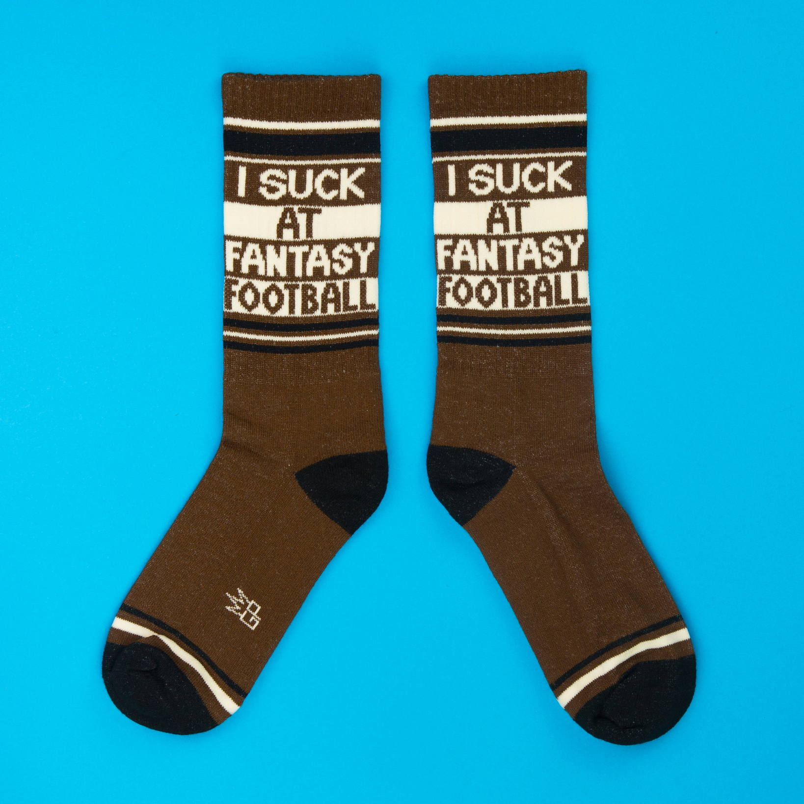 A pair of brown crew socks with "I Suck At Fantasy Football" text, laid flat on a blue background.