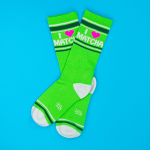 Two 'I Heart Matcha' crew socks crossed on a bright blue background, showing the text and striped cuffs.