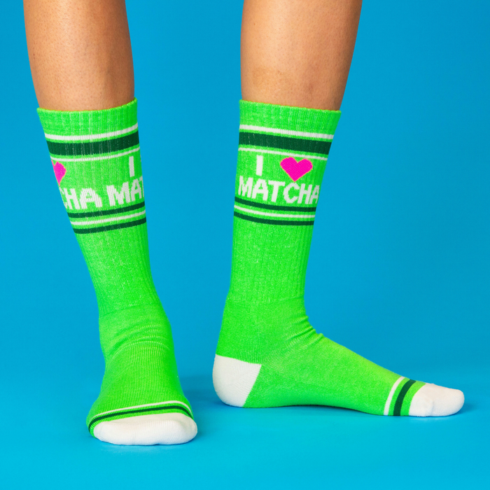 A person wearing bright green 'I Heart Matcha' crew socks, standing on a blue surface, showing the design.