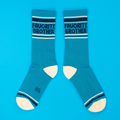 Two teal 'Favorite Brother' crew socks laid flat side-by-side on a bright blue background, showing full design.