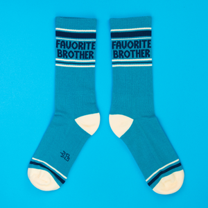 Two teal 'Favorite Brother' crew socks laid flat side-by-side on a bright blue background, showing full design.