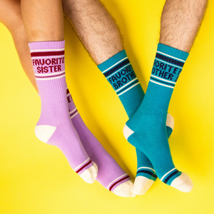 Two pairs of legs, one in lavender 'Favorite Sister' socks, other in teal 'Favorite Brother' socks on yellow.