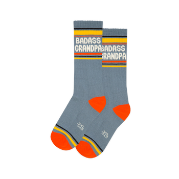 Pair of grey-blue crew socks with white "BADASS GRANDPA" text, yellow cuffs, orange heels & toes, and a grey logo.