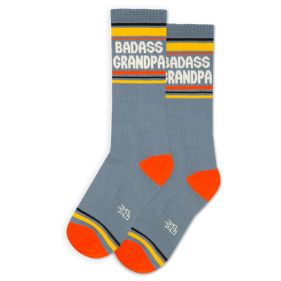 Pair of grey-blue crew socks with white "BADASS GRANDPA" text, yellow cuffs, orange heels & toes, and a grey logo.