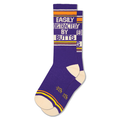 A pair of purple crew socks with "EASILY DISTRACTED BY BUTTS" text in white, orange, and cream stripes.