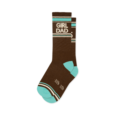 Brown crew socks with 'GIRL DAD' in white lettering, bordered by teal and off-white stripes. Features teal toe and heel, plus small white crown shapes.