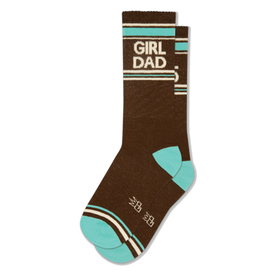 Brown crew socks with 'GIRL DAD' in white lettering, bordered by teal and off-white stripes. Features teal toe and heel, plus small white crown shapes.