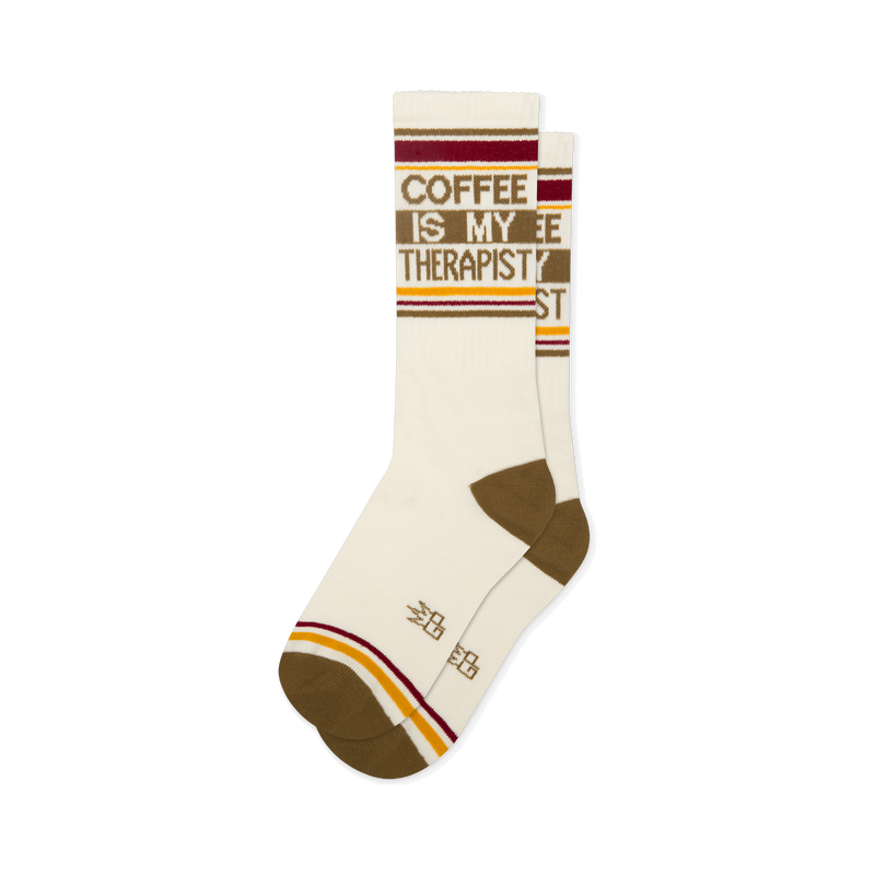 Off-white crew socks reading COFFEE IS MY THERAPIST in brown. Features brown heels, toes, and retro red and yellow stripes.
