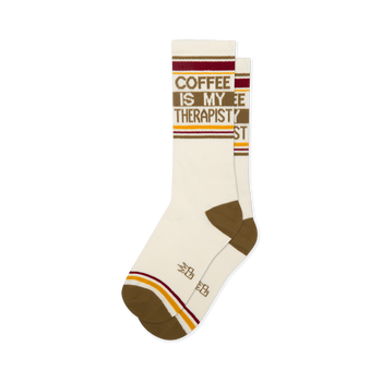 Off-white crew socks reading COFFEE IS MY THERAPIST in brown. Features brown heels, toes, and retro red and yellow stripes.