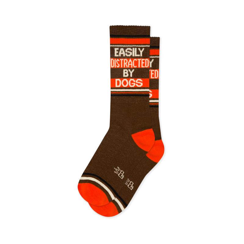 Brown crew socks with orange heel and toe. Bold white and orange text reads EASILY DISTRACTED BY DOGS between thin stripes.