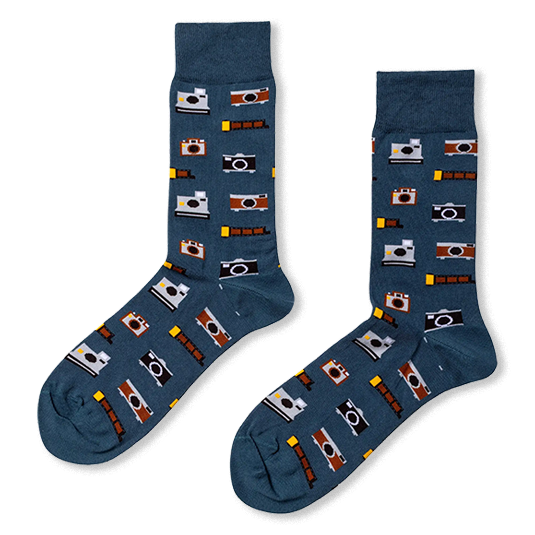 Two dark blue socks laid flat, featuring a repeating pattern of grey instant cameras, brown vintage cameras, and film strips.