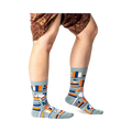 Person standing wearing sage green bookshelf crew socks, showing the full pattern on both feet and lower legs.