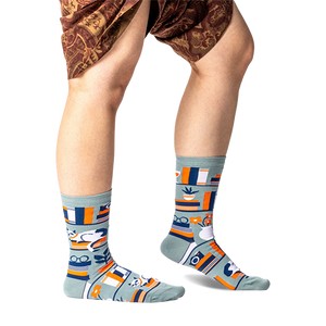 Person standing wearing sage green bookshelf crew socks, showing the full pattern on both feet and lower legs.