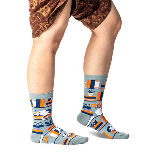 Person standing wearing sage green bookshelf crew socks, showing the full pattern on both feet and lower legs.