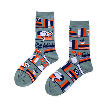 Pair of crew socks in sage green with a bookshelf pattern. Design includes books, a white cat, plants, and reading glasses.