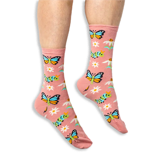 [lf] Someone wearing dusty pink socks with a colorful butterfly and caterpillar pattern against a solid black background.