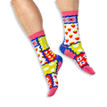 [lf] A person wearing bright patchwork socks featuring strawberries, tulips, polka dots and stripes on a black background.
