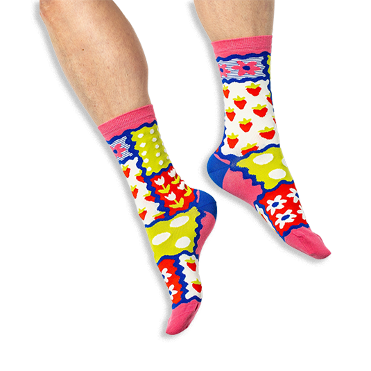[lf] A person wearing bright patchwork socks featuring strawberries, tulips, polka dots and stripes on a black background.