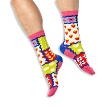 [lf] A person wearing bright patchwork socks featuring strawberries, tulips, polka dots and stripes on a black background.
