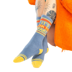 Close-up shot: 'It's Ok to Fart' socks on a person's legs; the focus is on the socks' design and texture.
