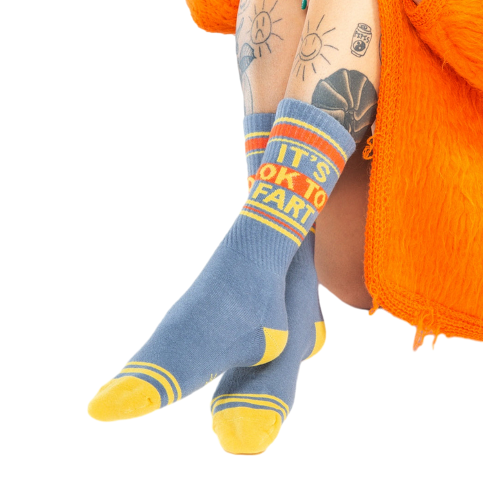 Close-up shot: 'It's Ok to Fart' socks on a person's legs; the focus is on the socks' design and texture.