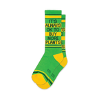 Pair of green and yellow crew socks with the text 'It's Always Ok To Buy More Plants' in black.  Features yellow and green stripes at the cuff.