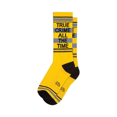 A pair of yellow crew socks with grey stripes and 'TRUE CRIME ALL THE TIME' in black lettering.  Black cuffs and toes.