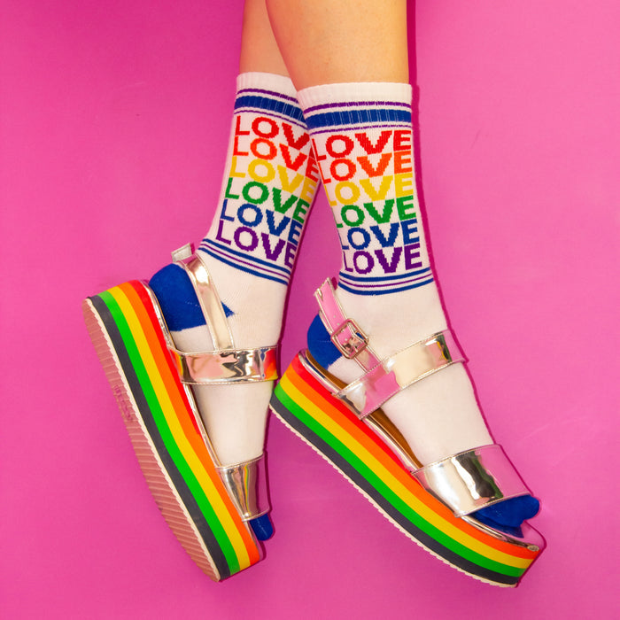 A pair of white socks with the word love displayed in rainbow colors.