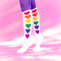 Lifestyle photo: Rainbow Hearts socks on a model's legs against a pink background. [lf]