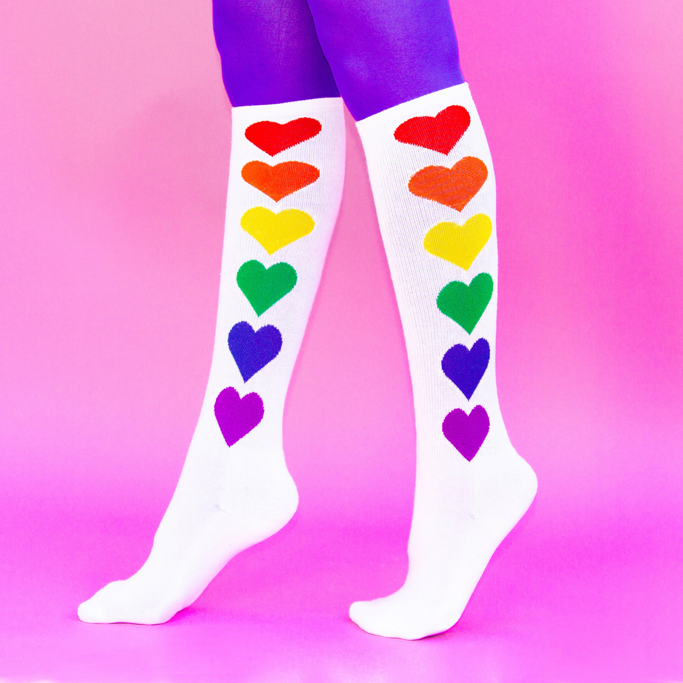Lifestyle shot: Rainbow Hearts socks on legs, against a pink background. [lf]