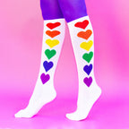 Lifestyle shot: Rainbow Hearts socks on legs, against a pink background. [lf]