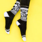 Lifestyle shot: A person's legs wearing the 'I Give The Best Blow Jobs' socks against a yellow background.