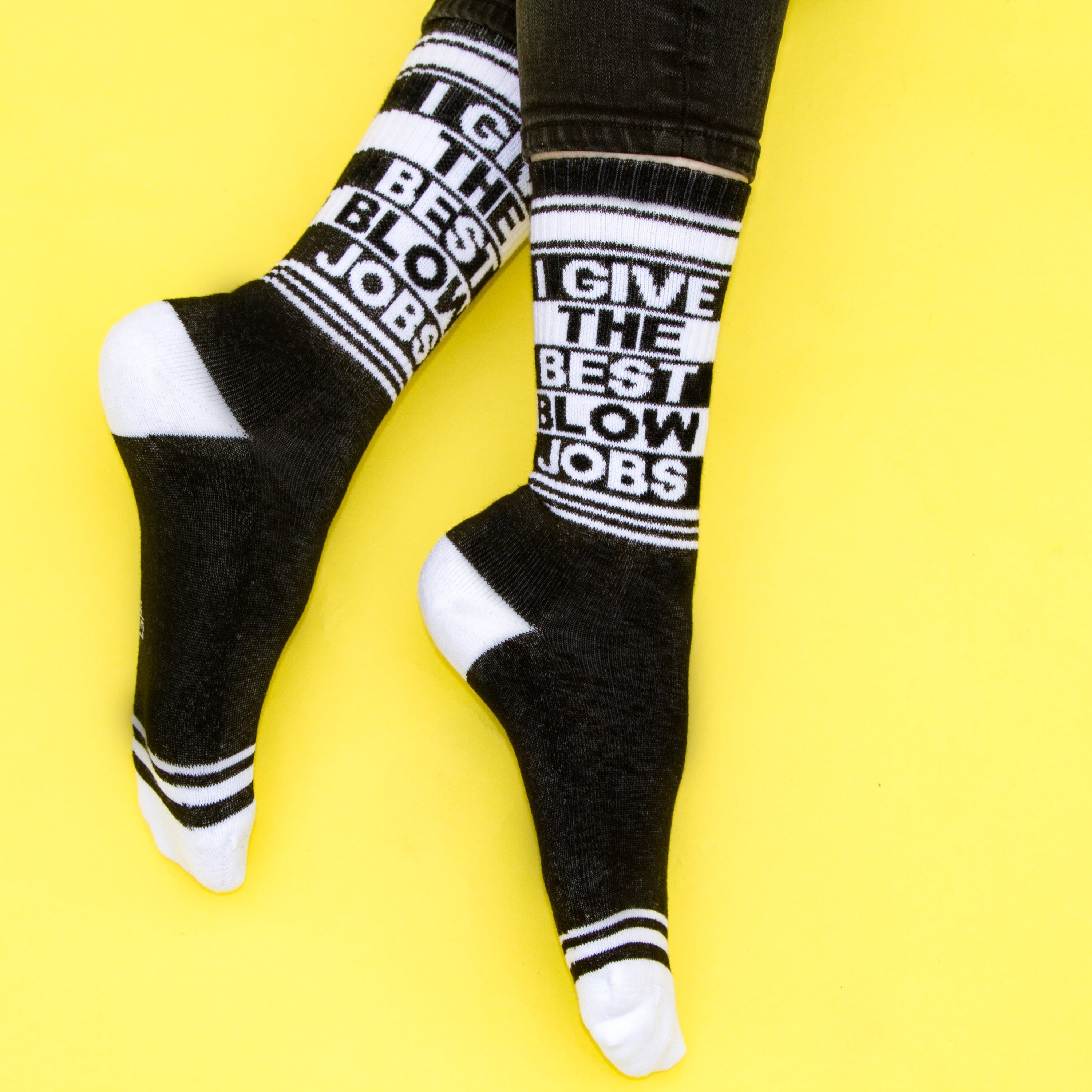 Lifestyle shot: A person's legs wearing the 'I Give The Best Blow Jobs' socks against a yellow background.