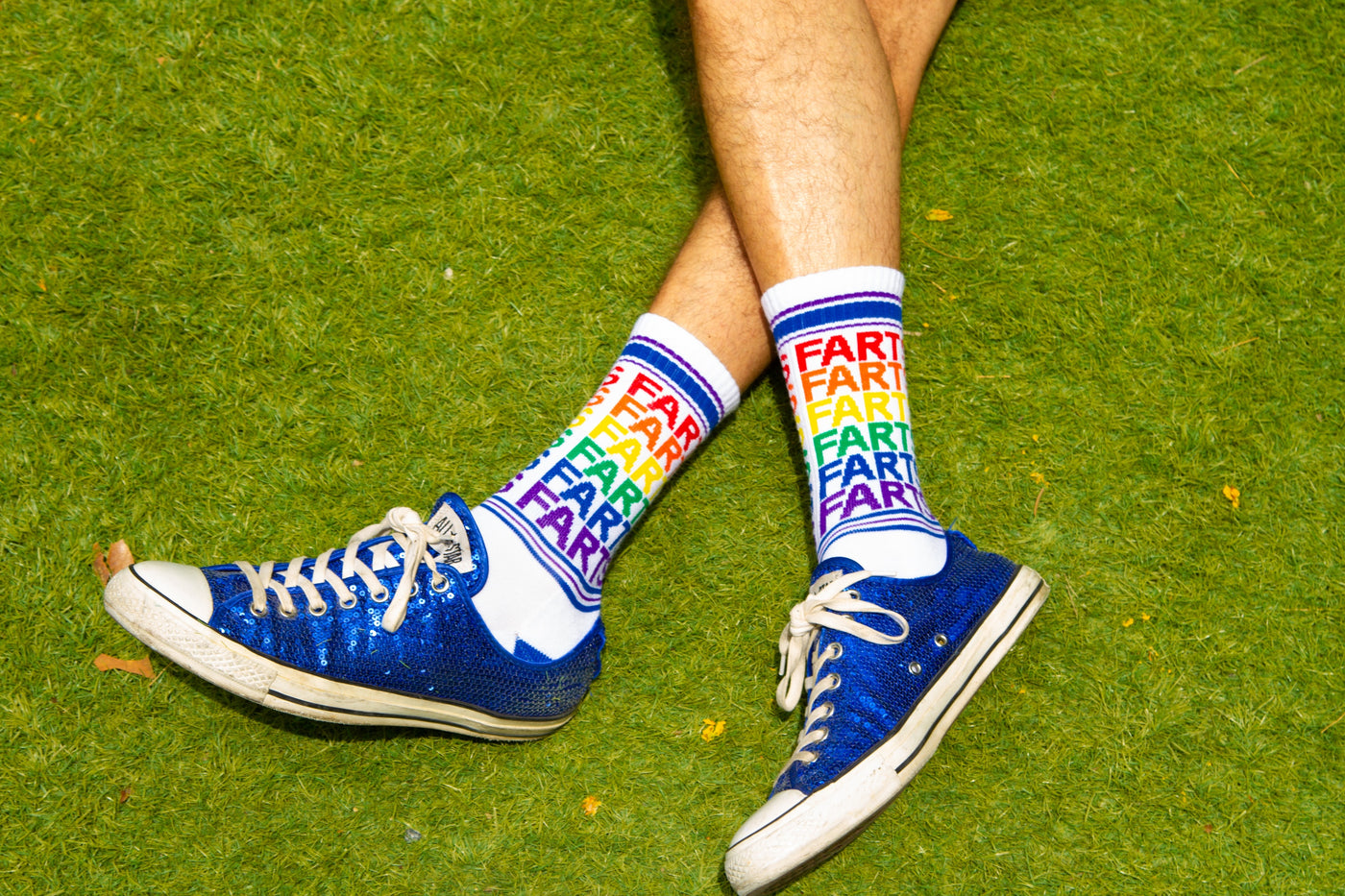 Flat lay image showing the 'Farts' socks worn with blue sparkly sneakers on grass. [lf]