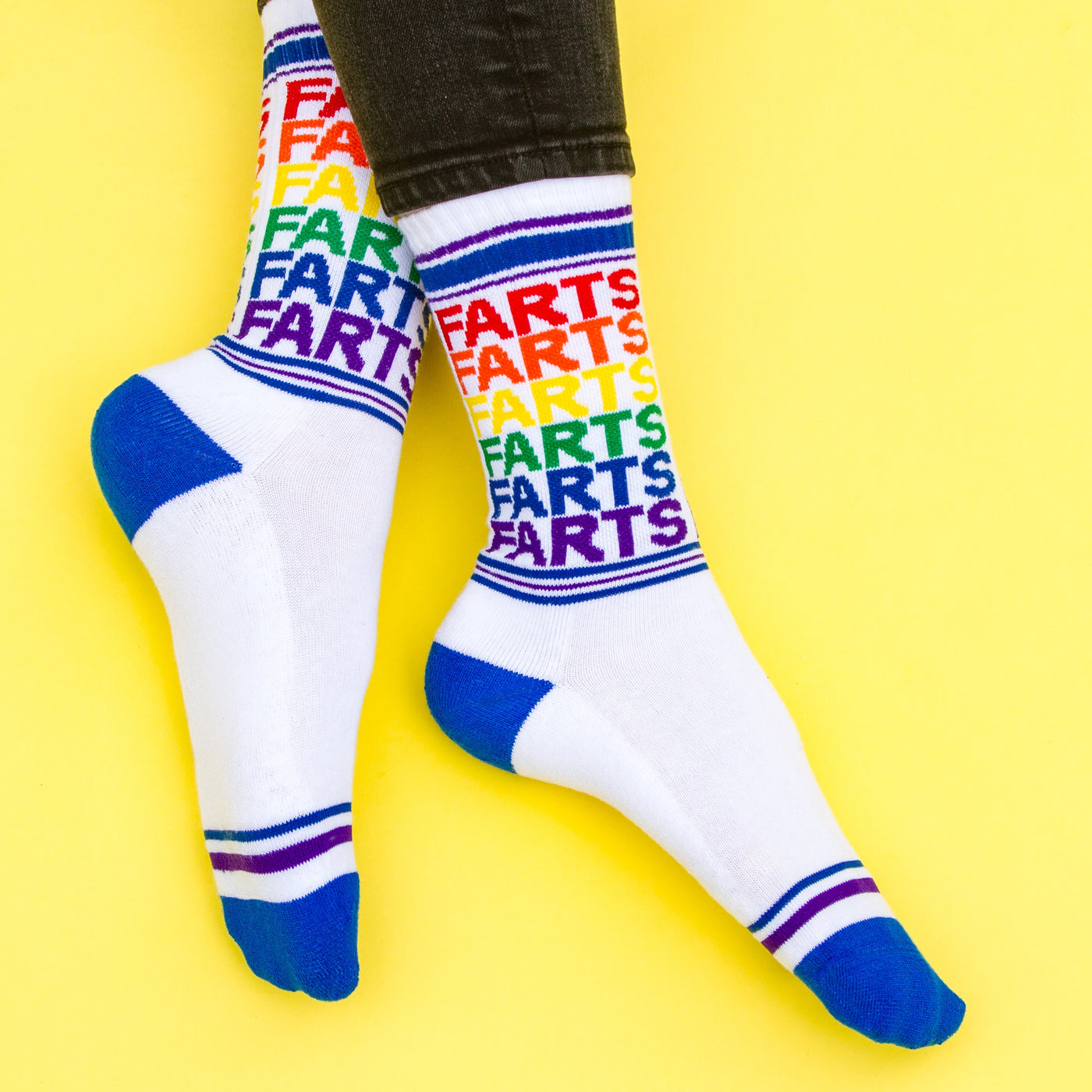 Close-up shot of 'Farts' socks on a yellow background, showcasing the rainbow design and blue cuffs. [lf]