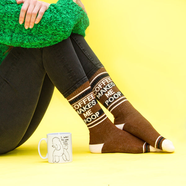 Lifestyle photo showing a person wearing the 'Coffee Makes Me Poop' socks with a coffee mug. [lf]