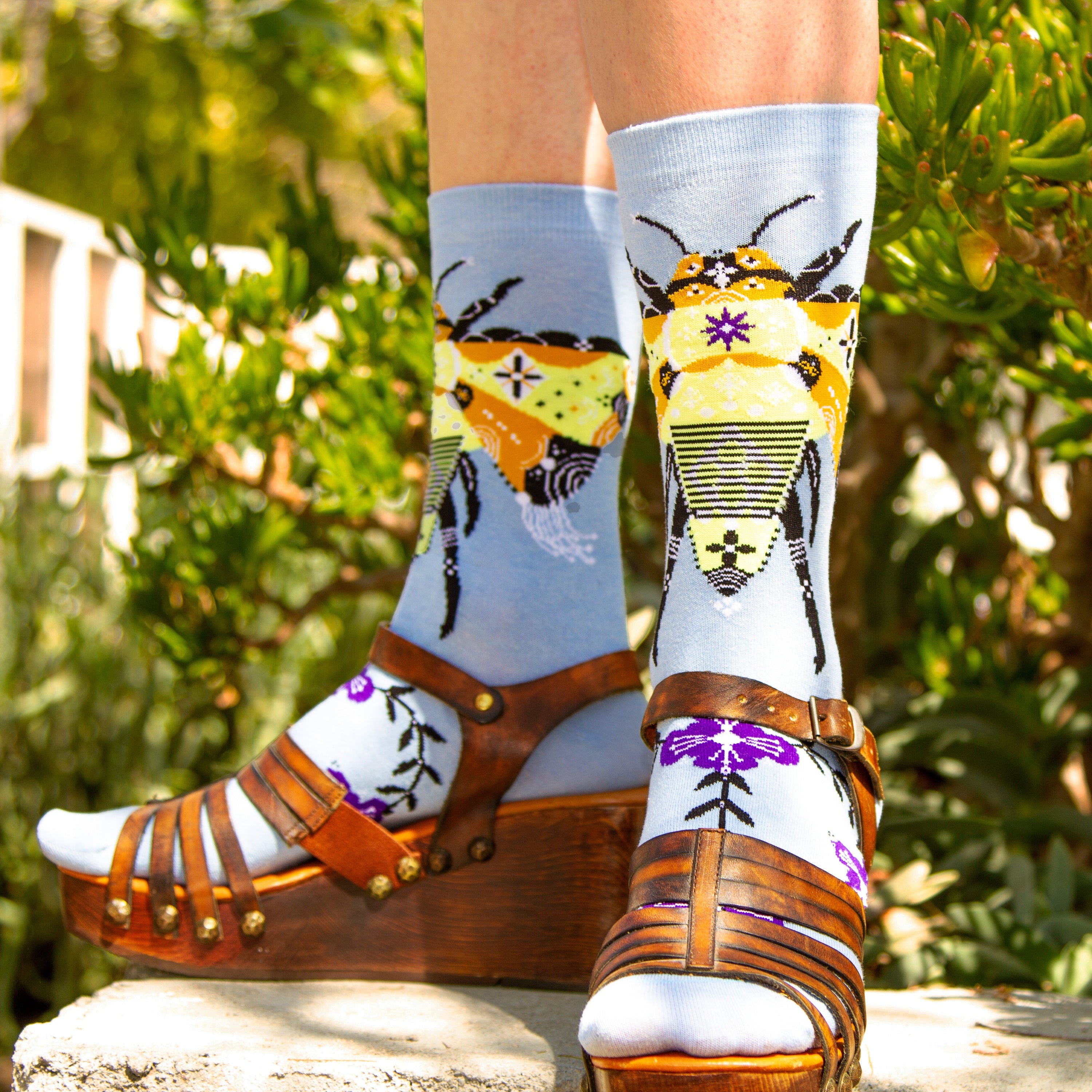 Lifestyle shot of a person wearing the Bee & Flowers socks with brown wedge sandals. [lf]