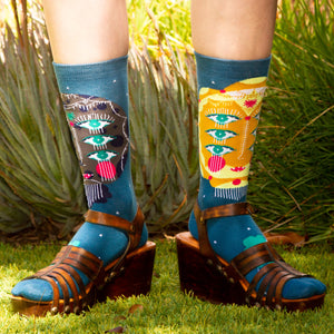 A pair of blue socks with a pattern of cartoon faces with three eyes on each face.