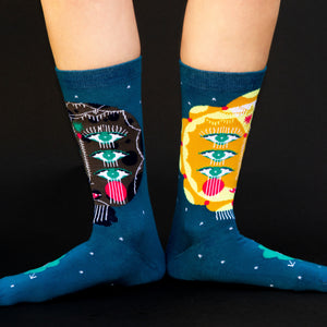 A pair of blue socks with a pattern of cartoon faces with three eyes on each face.